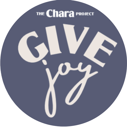 A round graphic with a dark gray background featuring the words "The Chara Project" at the top and "GIVE joy" in large, light-colored, bold and script fonts in the center.
